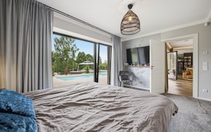 A bedroom with a large bed, a view of a swimming pool, and a television mounted on the wall. - Luxury Pool & Sauna Villa Roiu (Roiu)
