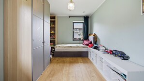 Een slaapkamer met een bed, een kledingkast, een bureau met speelgoed en een raam met gordijnen.