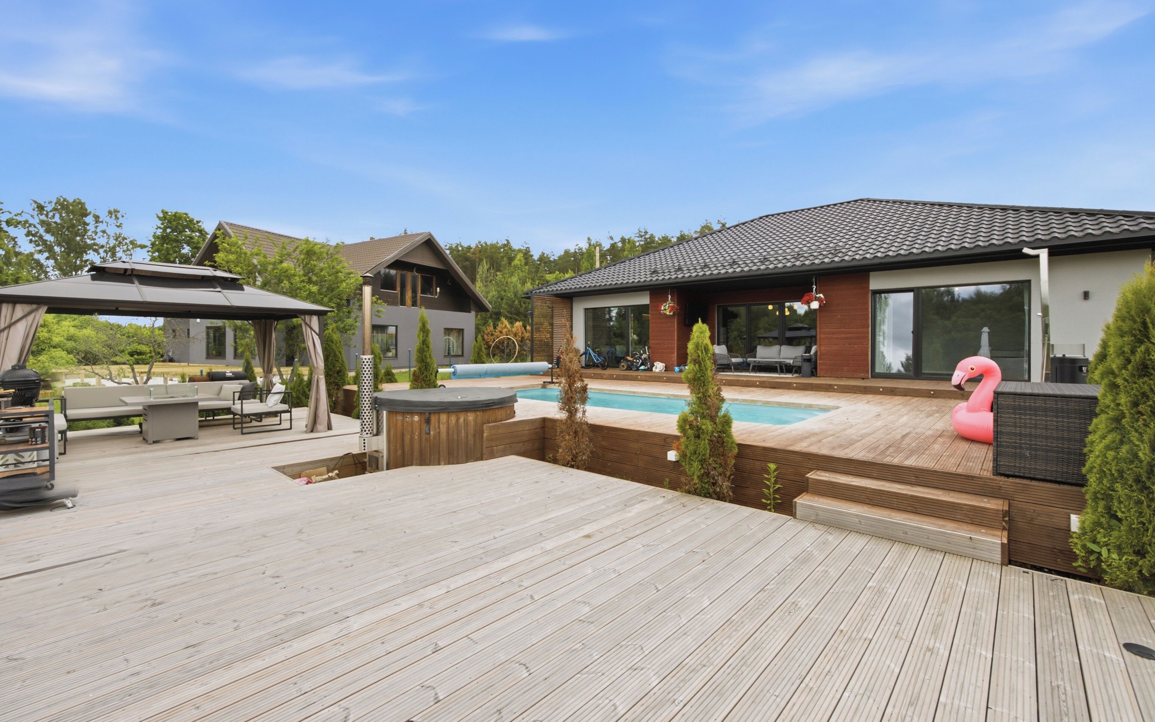 Un terrazzo in legno con vasca idromassaggio, piscina e una casa dal design moderno.