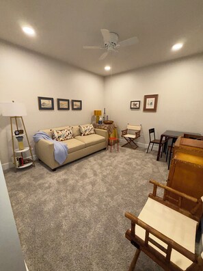 A living room with a sofa, a small table, a lamp, and a ceiling fan. - Refined Coastal Condo with Pool near Beach (Rehoboth Beach)
