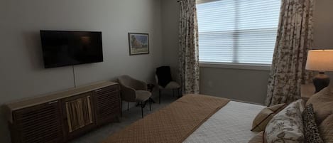 A bedroom with a bed, a television, a ceiling fan, a window with curtains, and a bedside table.