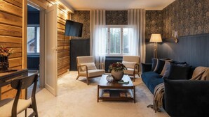 A cozy living room with a sofa, two armchairs, a coffee table with a vase, a flat-screen TV, and a window with curtains. - Skýra Retreat (Rovaniemi)