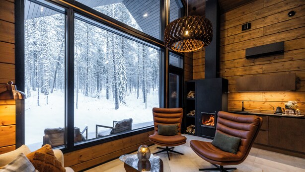 A cozy interior with a large window overlooking a snowy forest, a fireplace, leather armchairs, and a modern glass coffee table. - Skýra Retreat (Rovaniemi)