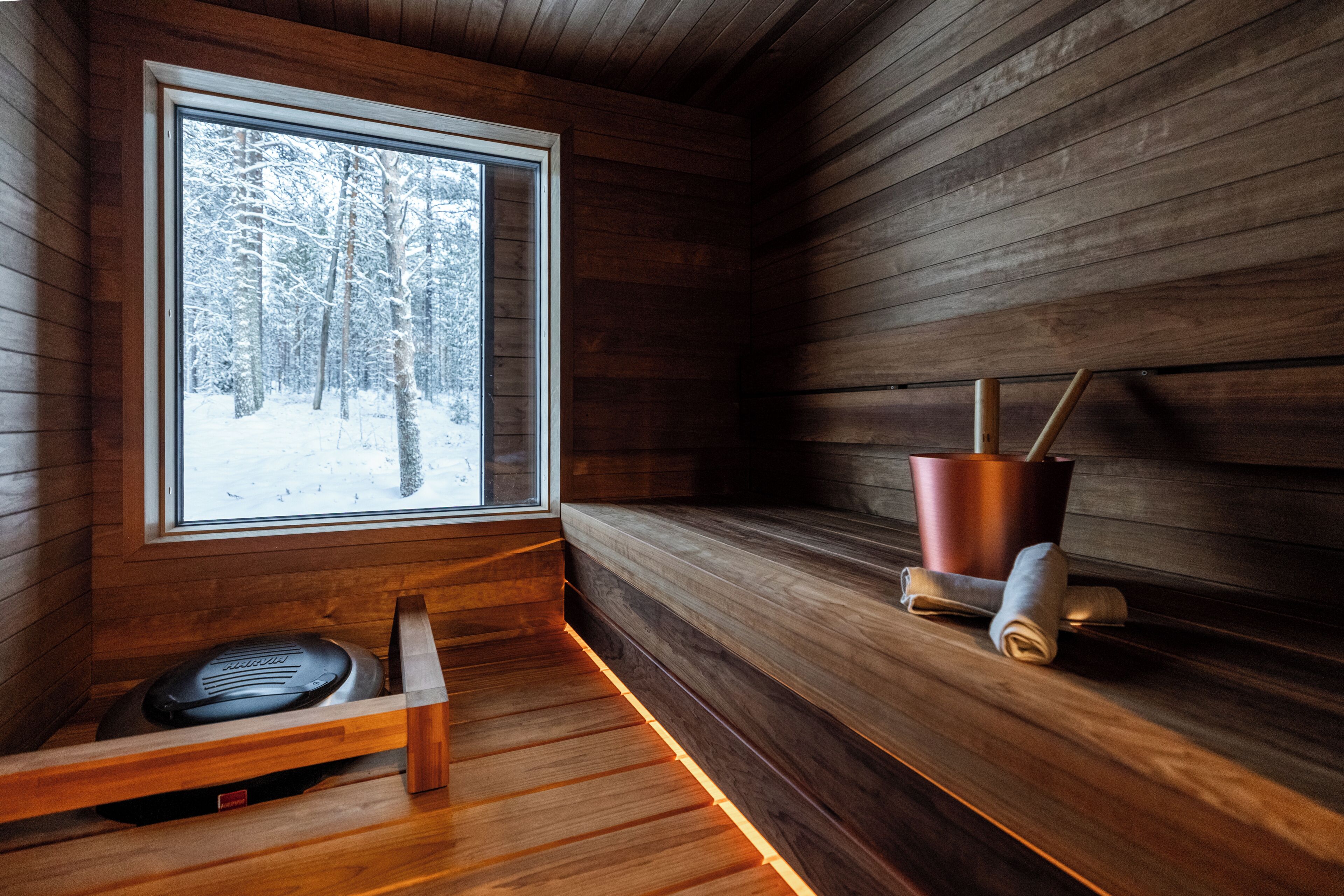 A wooden cabin interior with a bench, a window, and a metal bucket.