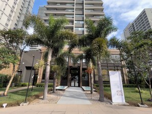 Un edificio moderno con una entrada central, rodeado de palmeras y un camino que lleva a ella.