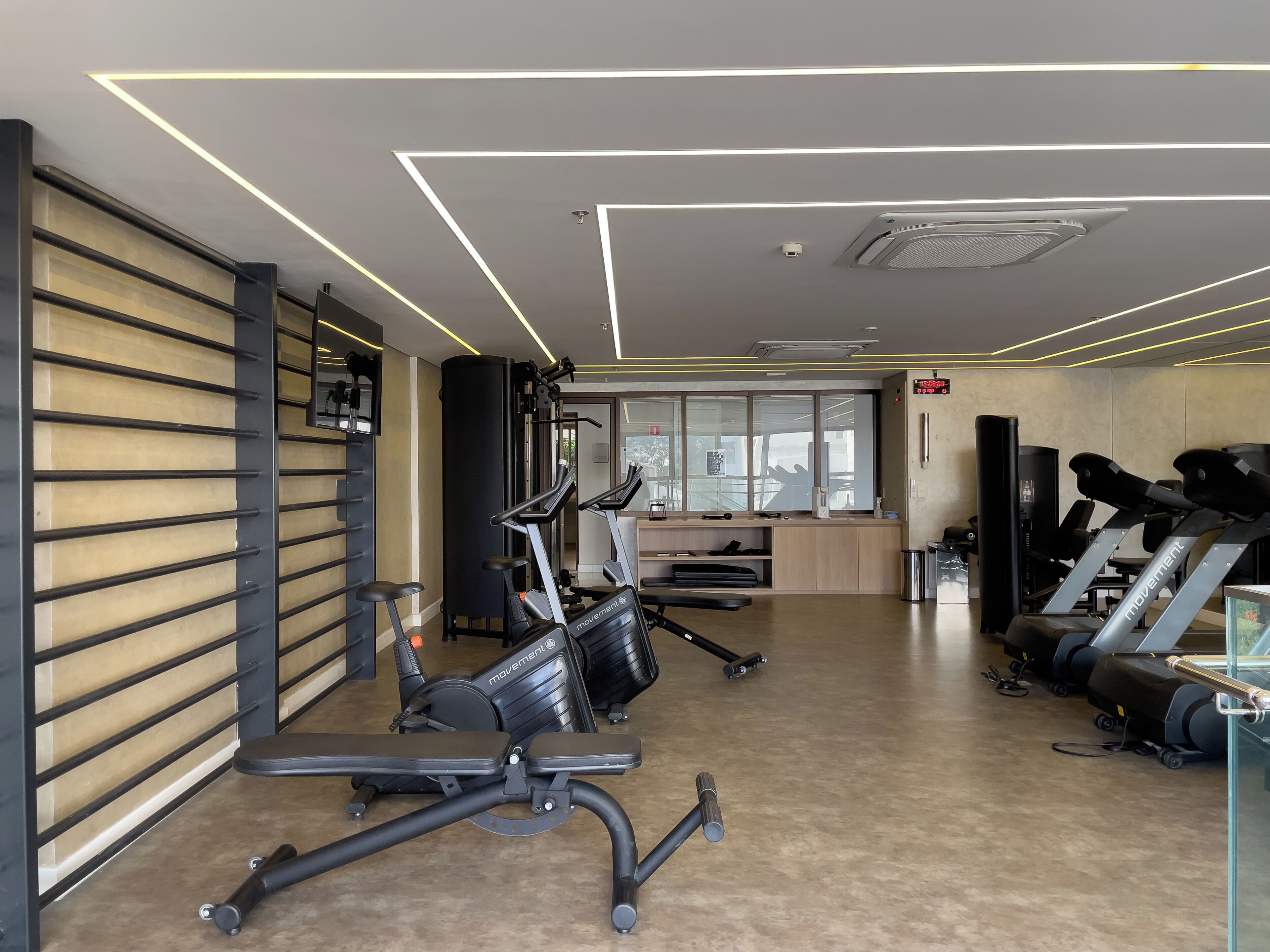 A gym with exercise equipment, a wall-mounted rack, and a digital display.