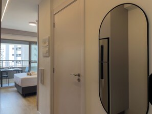 Un cuarto de hotel con cama, mesita de noche, espejo y vista de la ciudad a través de la ventana.