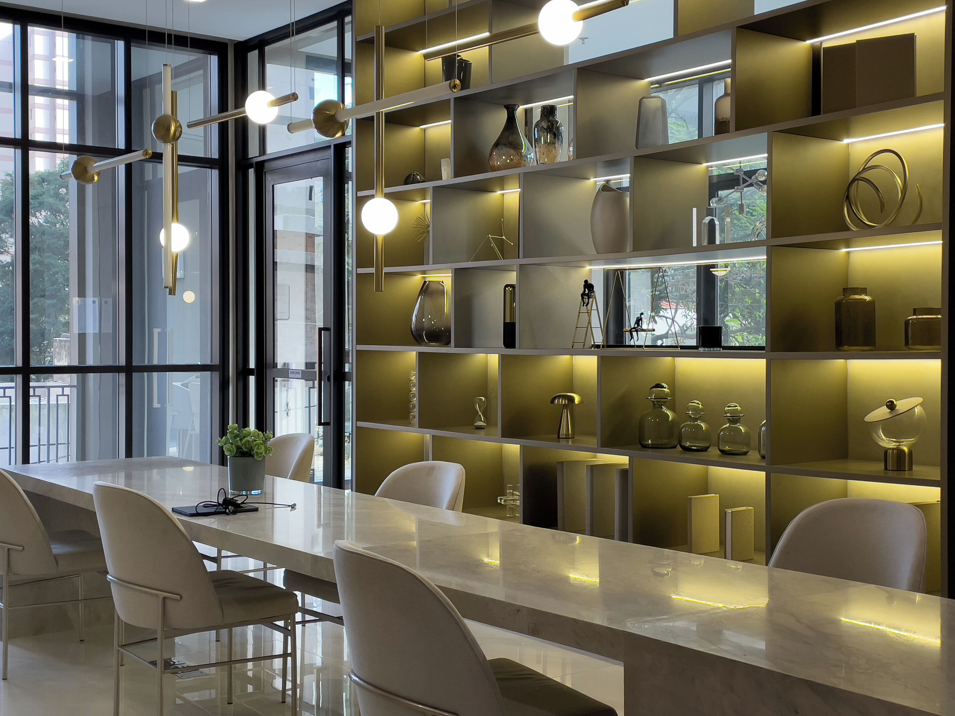 Un interior moderno con una larga mesa de comedor, múltiples sillas y una pared de estanterías con varios objetos decorativos.