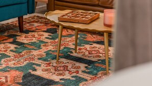 Een woonkamer met een bruine leren bank, een blauwe fauteuil, een vloerkleed met dessin, een houten bijzettafeltje met een spel, en een lamp op een tafeltje.