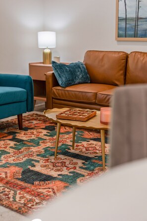 A living room with a brown leather sofa, a blue armchair, a patterned rug, a small wooden table with a board game, and a lamp on a side table. - 7 Bedrooms 6 Baths and more! (Lafayette)