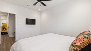 Een slaapkamer met een bed, een plafondventilator, een tv aan de muur en een deur naar een andere kamer.