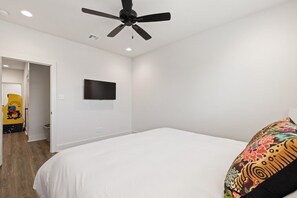 A bedroom with a bed, a ceiling fan, a mounted TV, and a door leading to another room. - 7 Bedrooms 6 Baths and more! (Lafayette)
