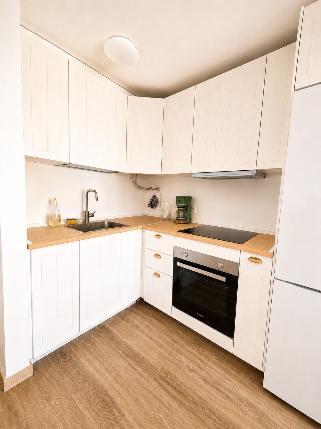 A kitchen with white cabinets, a stainless steel sink, a coffee maker, and a built-in oven.