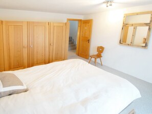 Ein Schlafzimmer mit einem Bett, einem Holzschrank, einem Stuhl und einem Spiegel an der Wand.