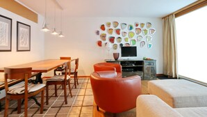 A modern living room with a dining area, a TV, and a wall with colorful face-shaped decorations.