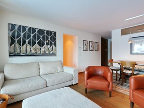 Ein Wohnzimmer mit einer Couch, einem Ledersessel, einem Esstisch mit Stühlen und einer Wand mit abstrakter Kunst.