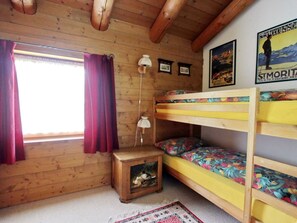 A wooden cabin room with bunk beds, a small table with a lamp, and a window with curtains. - Apartment Cign OG by Interhome (Celerina)