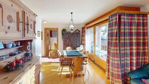 A cozy room with a dining table, chairs, a sofa, and a window with plaid curtains. - Apartment Ambretta OG by Interhome (St. Moritz)
