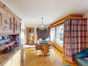 Ein gemütliches Zimmer mit Esstisch, Stühlen, einer Couch und einem Fenster mit Karomustertvorhängen.