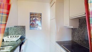 A compact kitchen with white cabinets, a granite countertop, and a poster on the wall. - Apartment Ambretta OG by Interhome (St. Moritz)