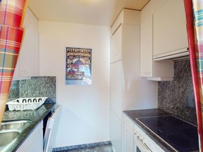 Eine kompakte Küche mit weißen Schränken, einer Arbeitsplatte aus Granit und einem Poster an der Wand.