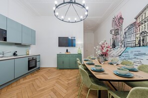 Uma cozinha moderna com área de jantar, uma televisão de tela plana fixada na parede e um mural de edifícios na parede adjacente.