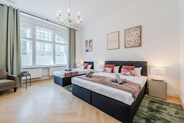 A hotel room with a large bed, two bedside tables, a sofa, and a window with curtains. - Prime Living Apartment, 135 m², City Center, 2 Bathrooms, Sleeps 8 (Berlin)