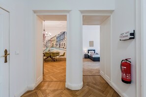 A hallway with a fire extinguisher mounted on the wall, a dining area with a table and chairs, and a bedroom with a bed and nightstand. - Prime Living Apartment, 135 m², City Center, 2 Bathrooms, Sleeps 8 (Berlin)