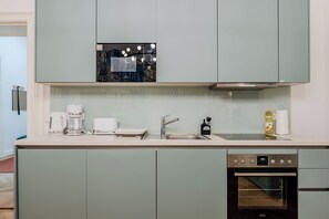 A modern kitchen with light green cabinets, a stainless steel sink, a coffee maker, a toaster, and an oven. - Prime Living Apartment, 135 m², City Center, 2 Bathrooms, Sleeps 8 (Berlin)
