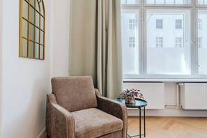 A room with a single armchair, a small table with a plant, a window with curtains, and a radiator. - Prime Living Apartment, 135 m², City Center, 2 Bathrooms, Sleeps 8 (Berlin)