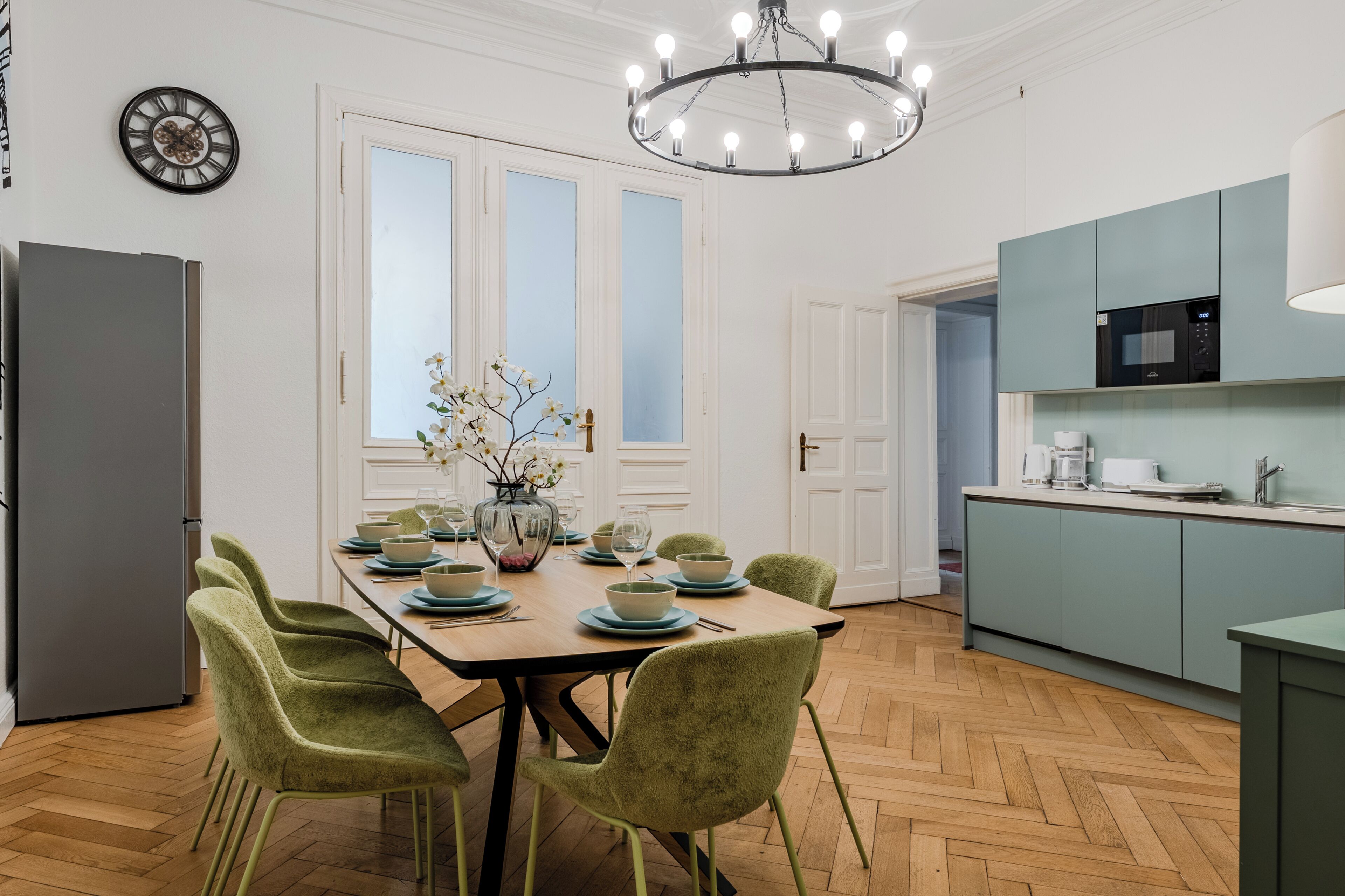 A modern kitchen with a dining area, featuring a chandelier, a refrigerator, and a microwave.