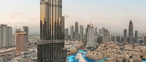 A high-rise building with a modern design, surrounded by other tall buildings and a water feature with fountains.