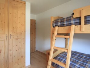 A bunk bed with a plaid-patterned mattress, a wooden wardrobe with two doors, and a small wooden stool. - Apartment Diala by Interhome (Zuoz)