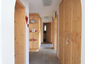A wooden hallway with a central wooden cabinet, a tiled floor, and a door on the right. - Apartment Diala by Interhome (Zuoz)
