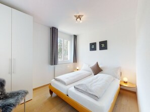 A modern bedroom with a double bed, a wardrobe, a window with curtains, and two wall-mounted picture frames. - Apartment Braschunauns 10 by Interhome (St. Moritz)
