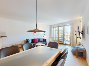 Una sala de estar moderna con comedor, ventanas amplias y vista al exterior.