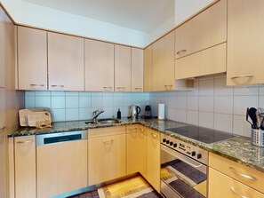 Una cocina con armarios de madera clara, lavavajillas integrado, estufa y pileta.