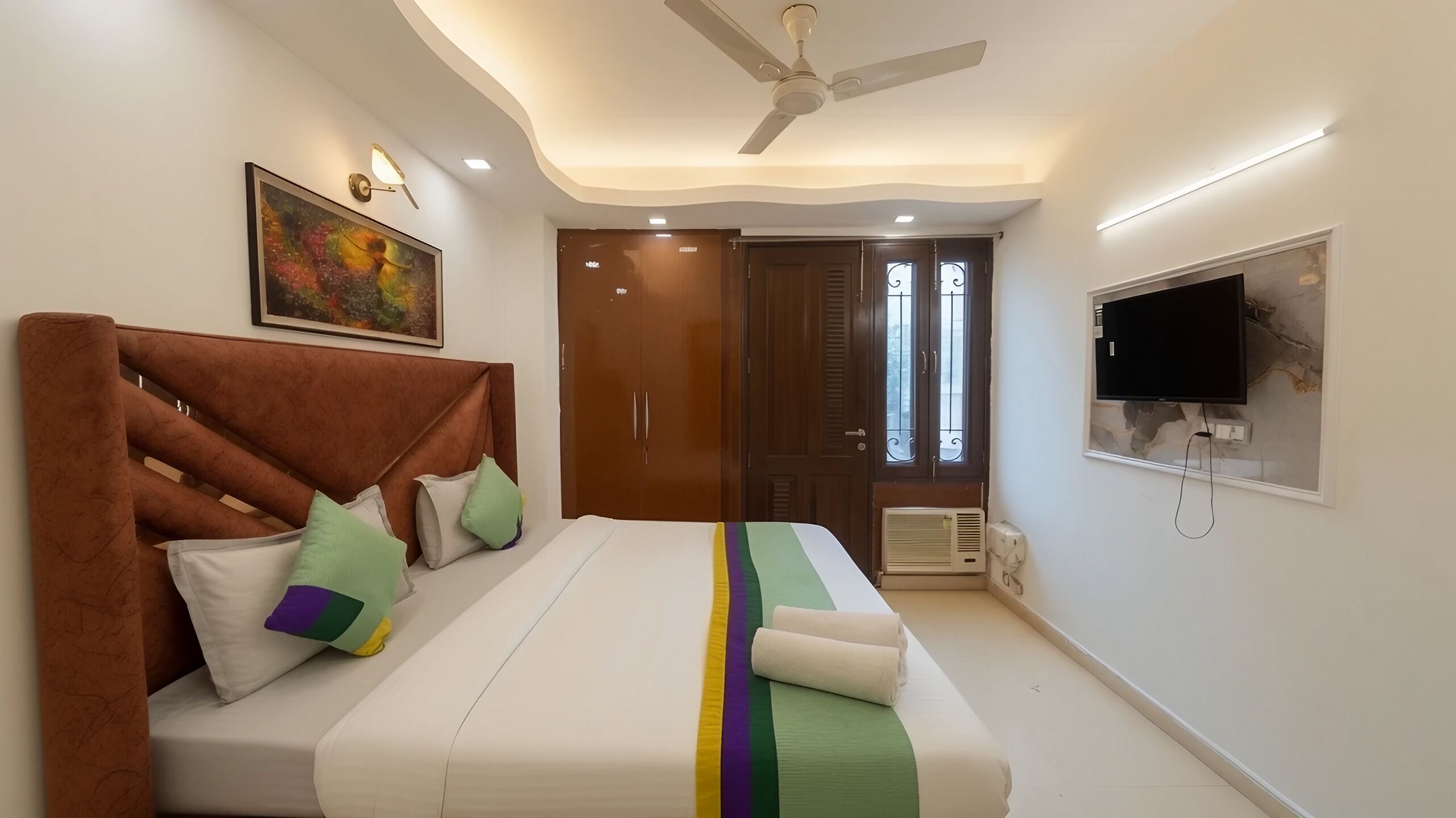 A bedroom with a bed, pillows, a ceiling fan, a TV, and a door.
