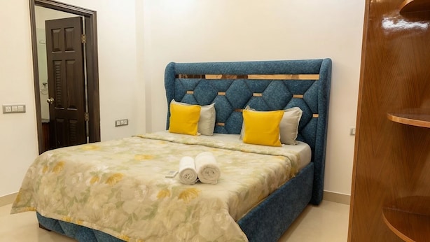 A bedroom with a bed, a wooden headboard, and a door. - Fortune Home Service Apartment E120 3BHK (Delhi)