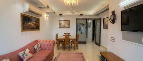 A living room with a sofa, a dining table with chairs, a television, and artwork on the walls.