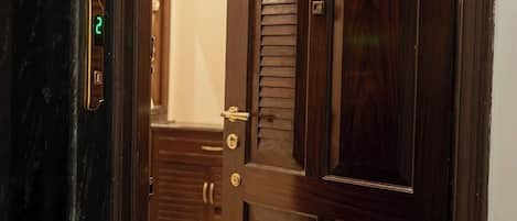 A wooden door with a keyhole and a lock, leading to a room with a marble floor and a wooden cabinet.