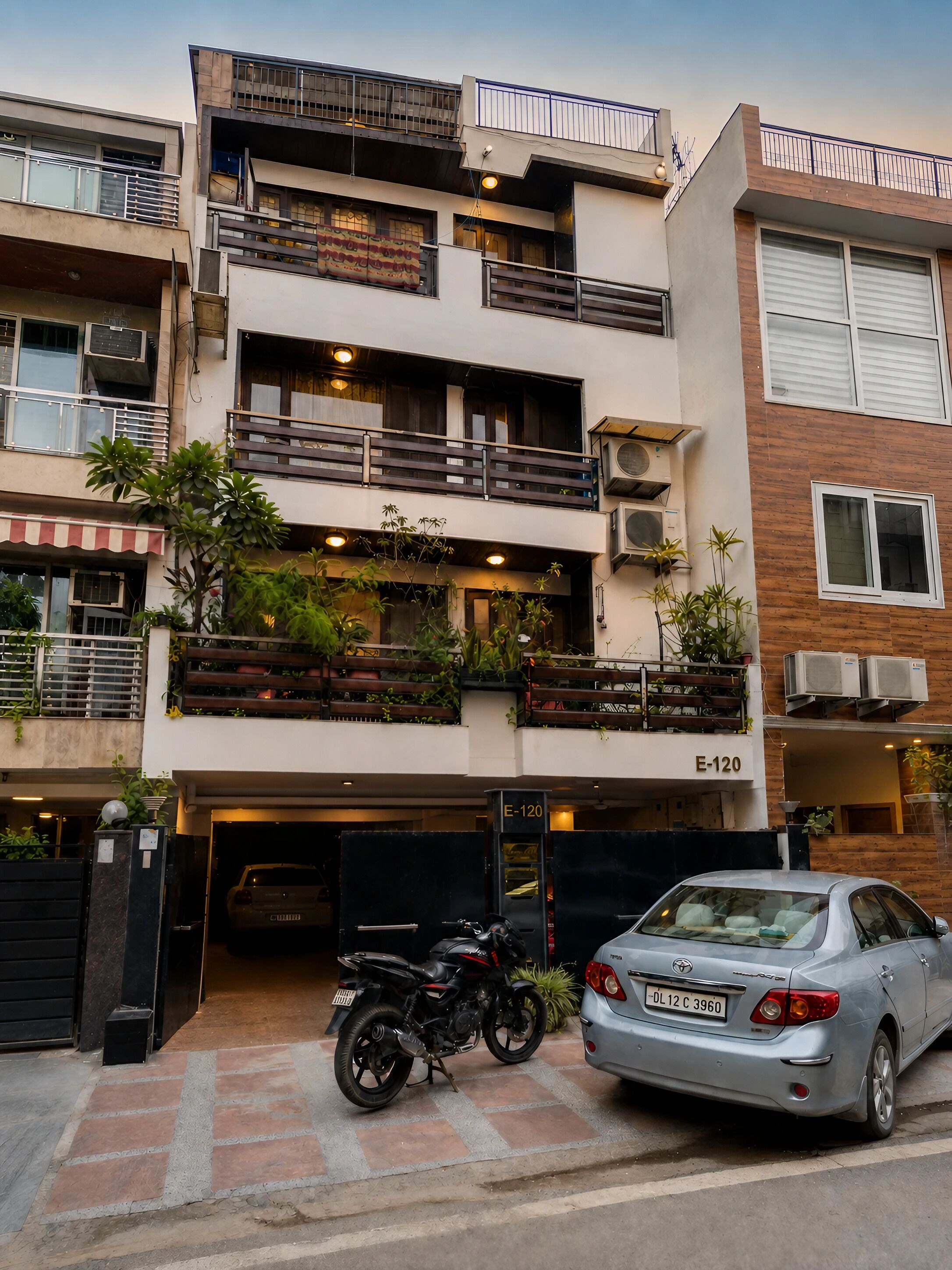 Un edificio residencial de varios pisos con balcones, unidades de aire acondicionado y un estacionamiento con una motocicleta y un automóvil.