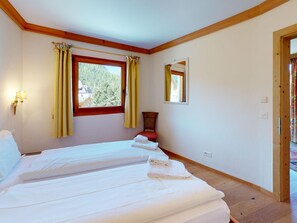 A bedroom with two beds, a window with curtains, a mirror, and a wooden floor. - Apartment Calimera by Interhome (Pontresina)