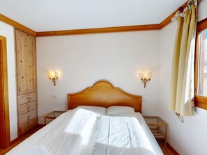 Une chambre à coucher avec une tête de lit en bois, deux tables de chevet avec des lampes, une armoire et une fenêtre avec des rideaux.