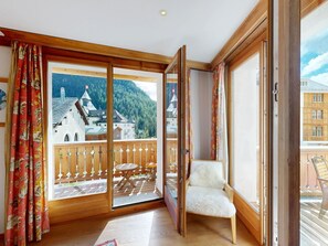 A room with a wooden balcony, a white chair, and a view of a mountain village. - Apartment Calimera by Interhome (Pontresina)