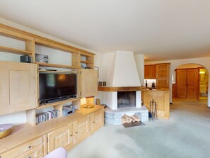 Ein Wohnzimmer mit Fernseher, Holzschränken, Kamin und Küchenzeile mit Holzschränken.