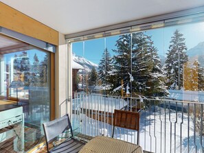 A balcony with a glass railing, a wicker chair, and a view of snow-covered trees and mountains. - Apartment Chalcherin 4 by Interhome (Celerina)