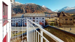 A residential area with a view of snow-capped mountains, a white building with a balcony, and a street with parked cars. - Apartment Crappun 3 by Interhome (Samedan)