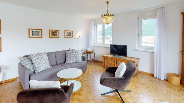 A modern living room with a grey sofa, two armchairs, a round coffee table, and a television on a wooden side table. - Apartment Crappun 3 by Interhome (Samedan)