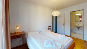 A hotel room with a bed, bedside table, lamp, and a bathroom visible through an open door. - Apartment Crappun 3 by Interhome (Samedan)